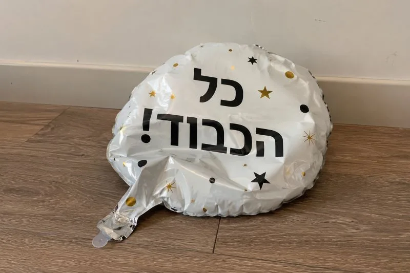 בלון כסוף מנופח למחצה על הרצפה, ועליו הכיתוב ״כל הכבוד!״